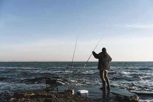 un pêcheur vêtu d'un manteau et d'un chapeau au bord de la mer