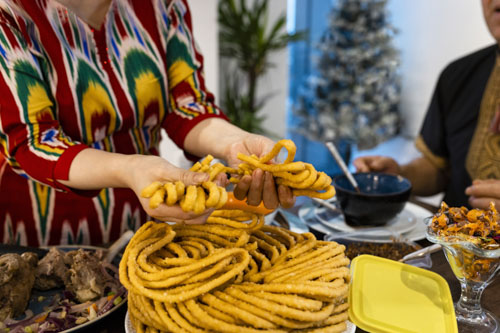 A Uyghur woman in traditional clothing breaking sangza, deep-fried noodles, to celebrate Eid al-Fitr.