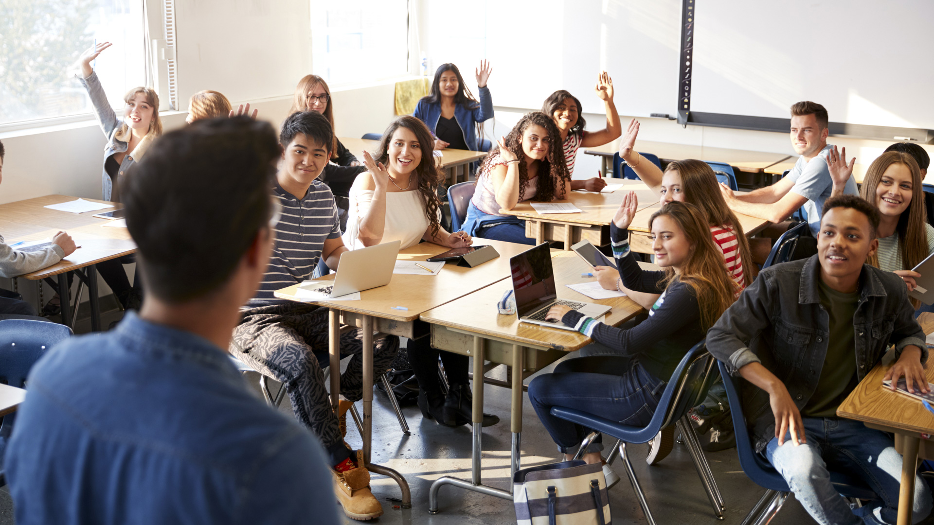 Rear View Of Male High School Teacher Standing At Front Of Class Teaching Lesson