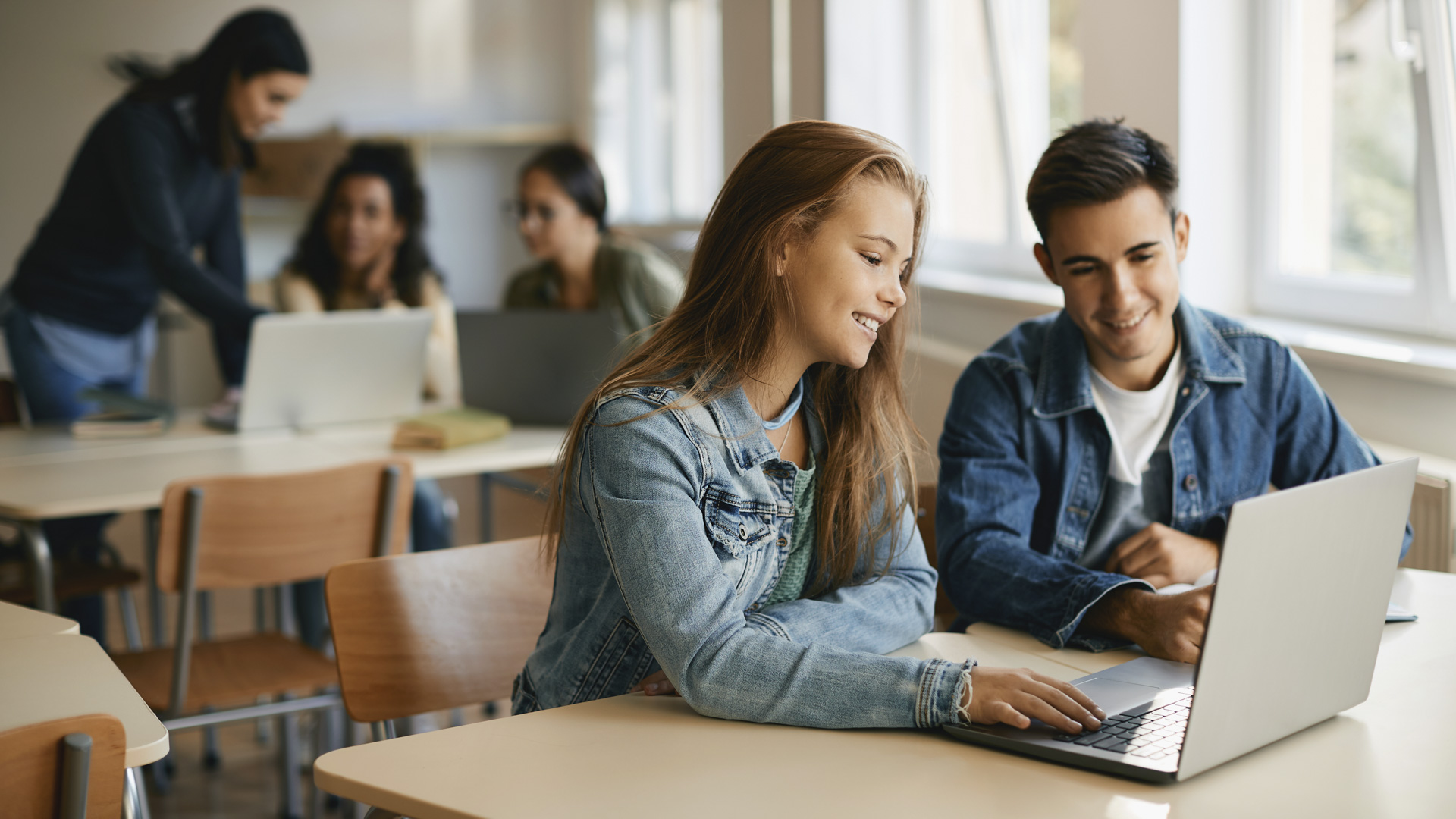 Happy teenage students cooperating while e-leaning on laptop during computer class.